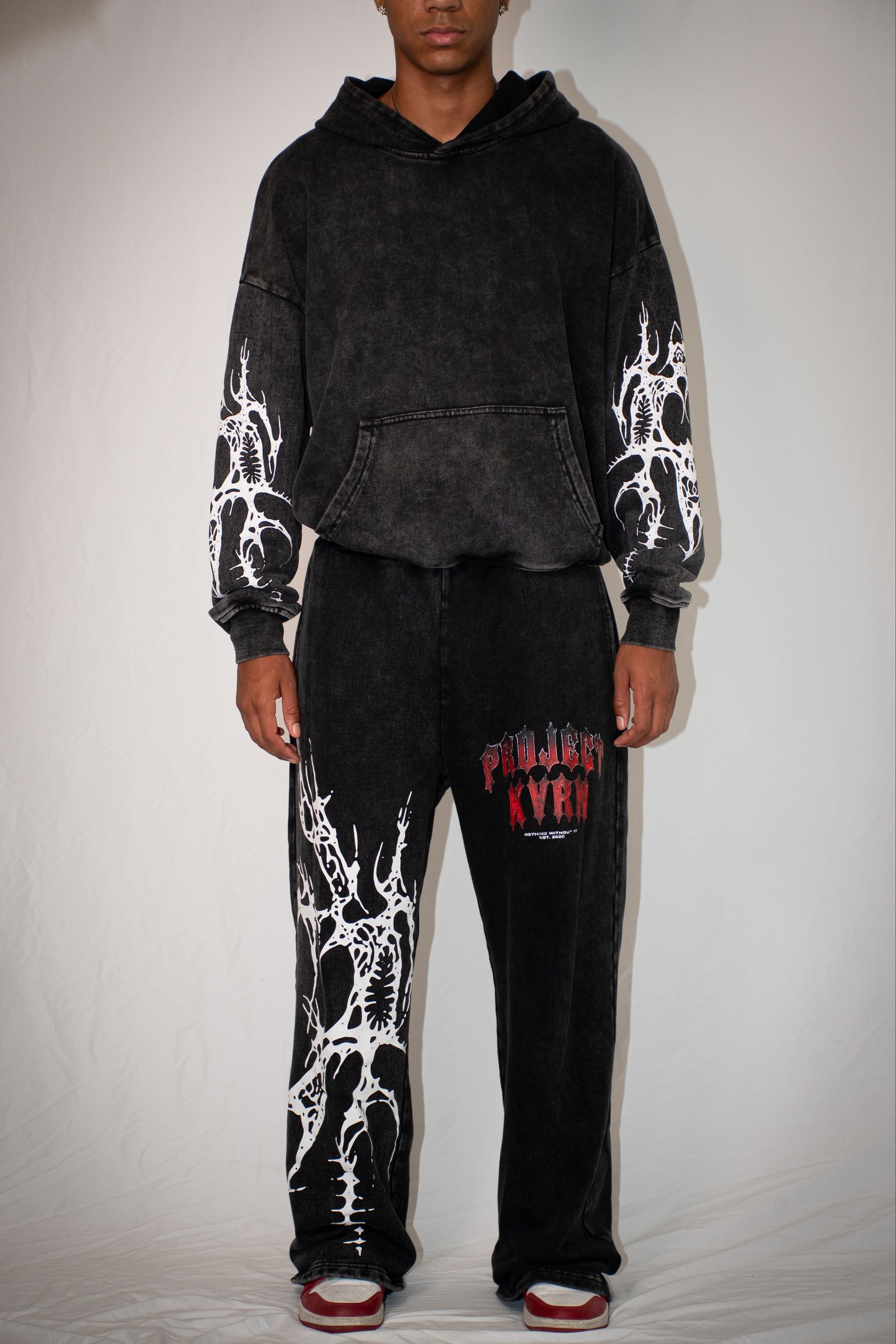Person wearing a black hoodie and pants with white designs on a plain background