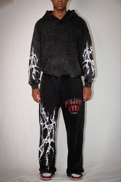 Person wearing a black hoodie and pants with white designs on a plain background