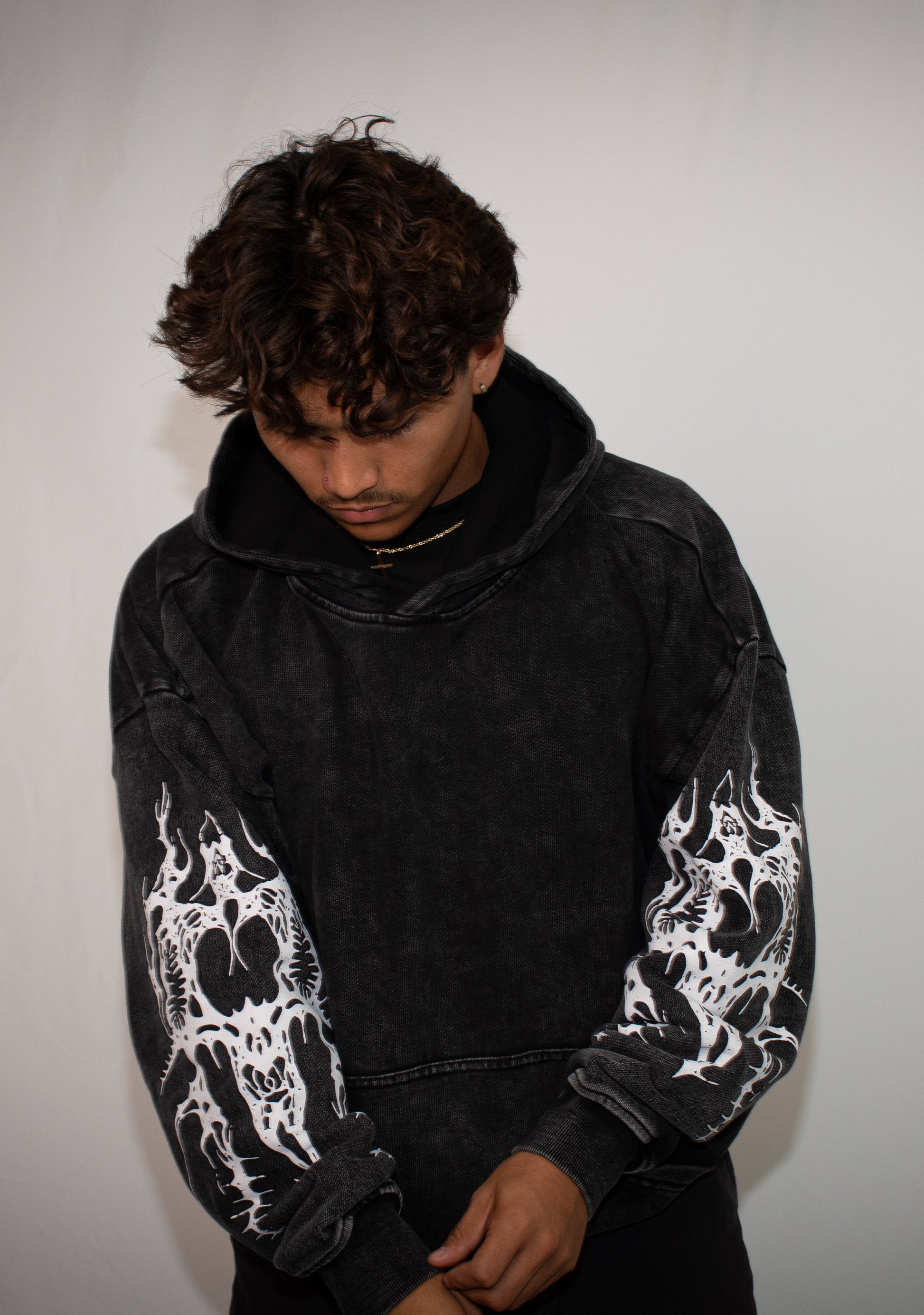Person wearing a black hoodie with white patterns on sleeves against a plain background