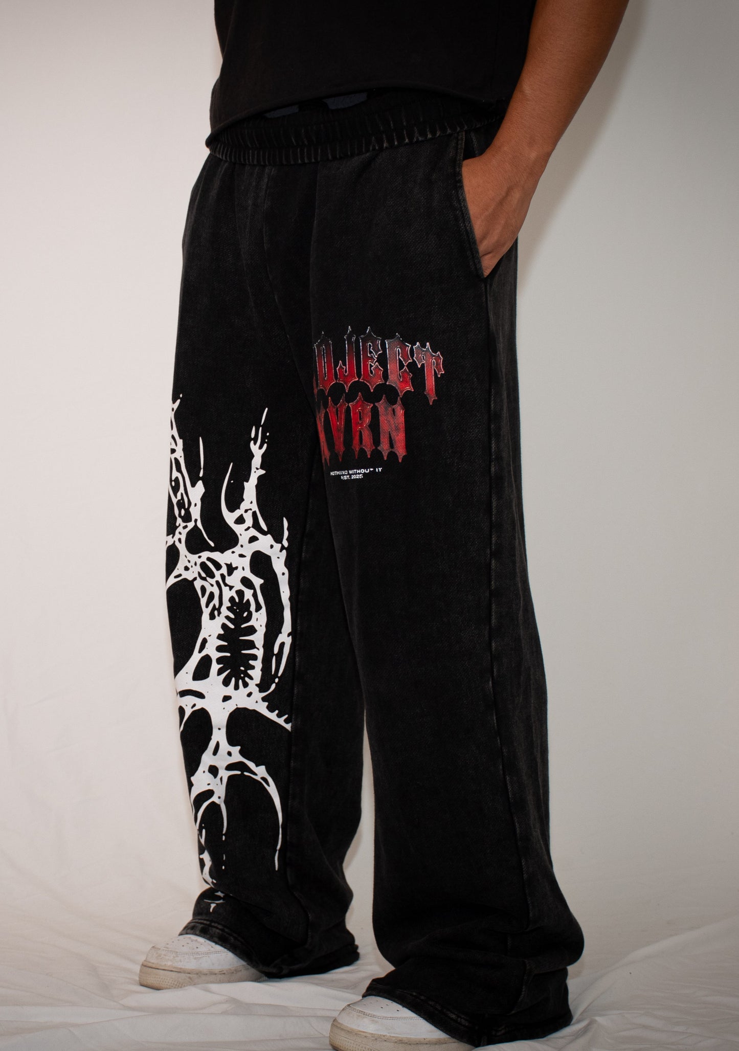 Person wearing black pants with white and red designs on a plain background